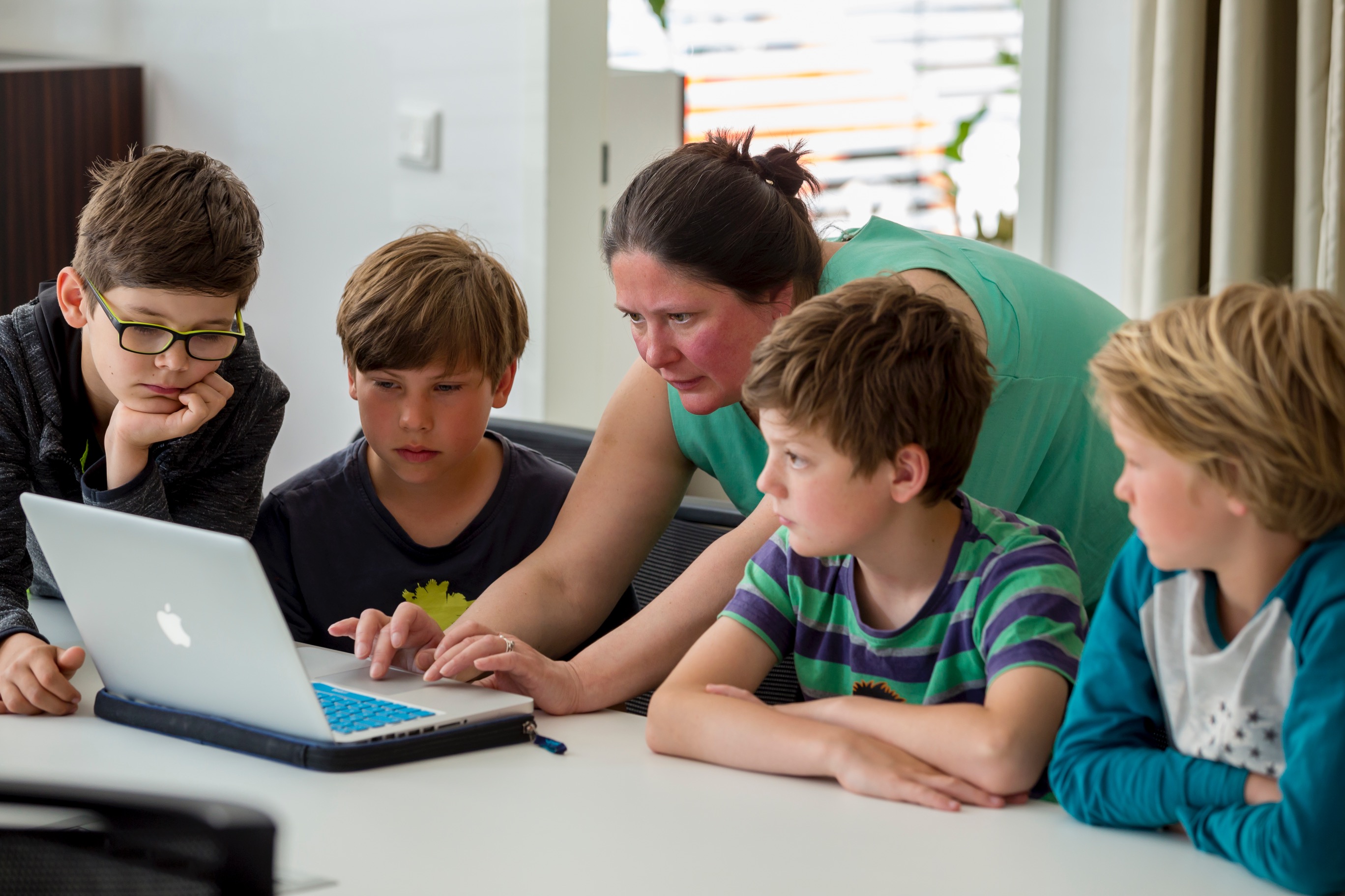 Betreuerin und vier Kinder, konzentriert über einen Laptop gebeugt