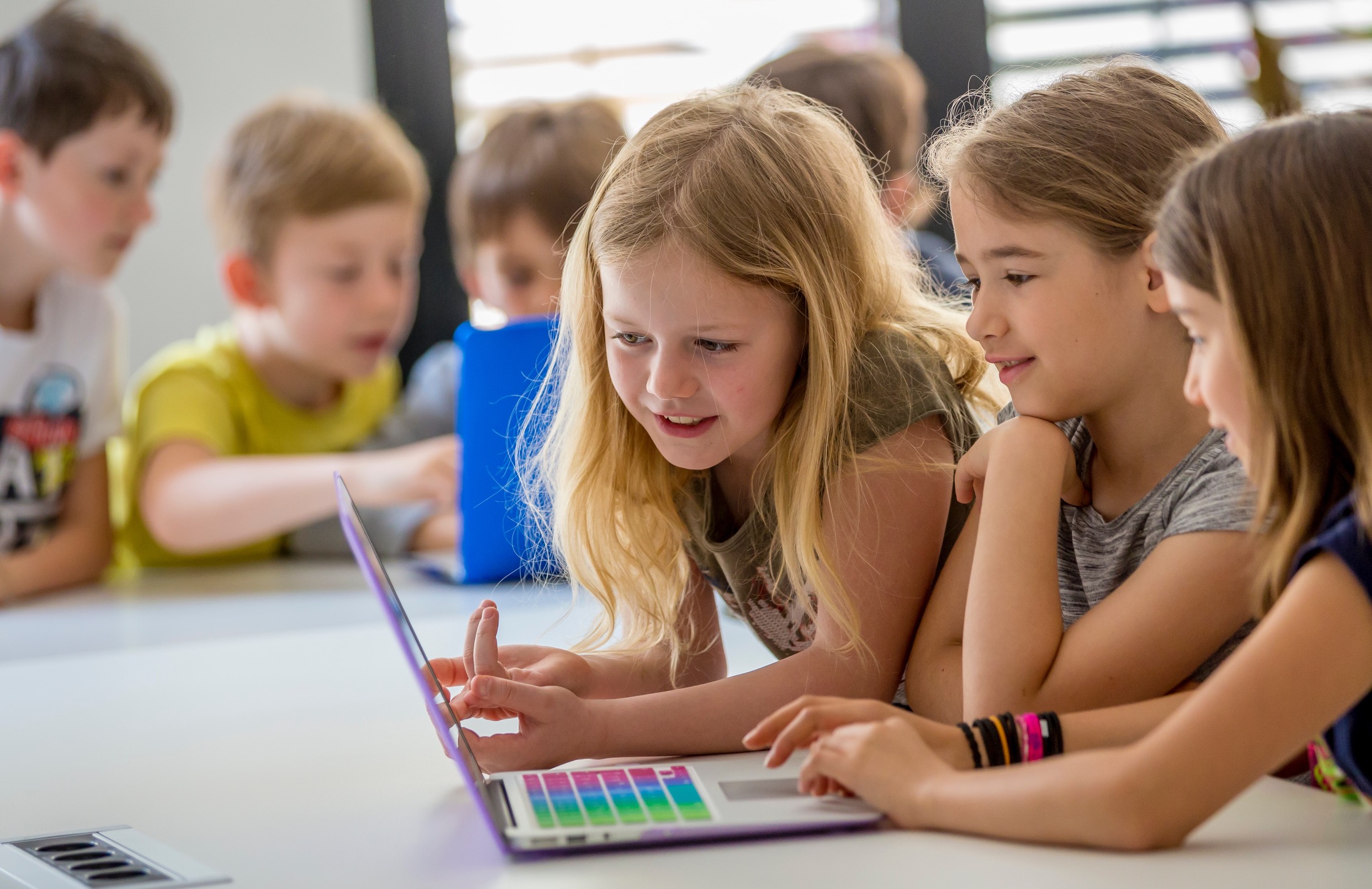 Zwei Kinder programmieren lächelnd an einem Laptop mit bunter Tastatur
