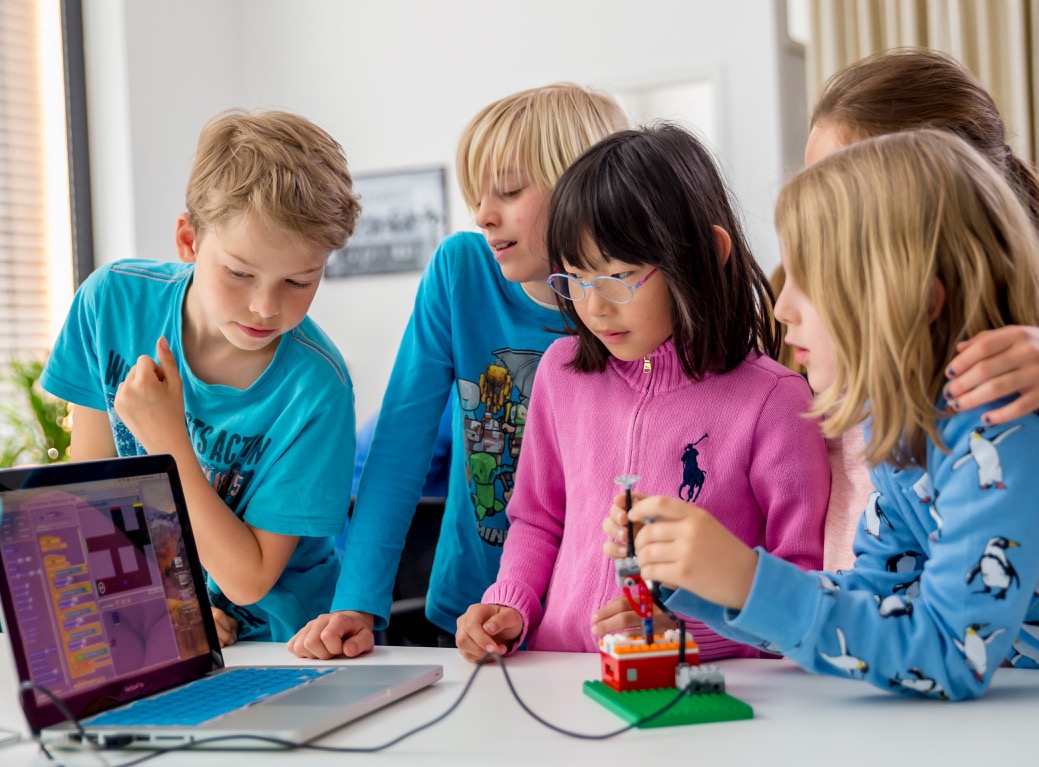 Kinder bauen gemeinsam einen Lego-Roboter neben einem Laptop mit Scratch